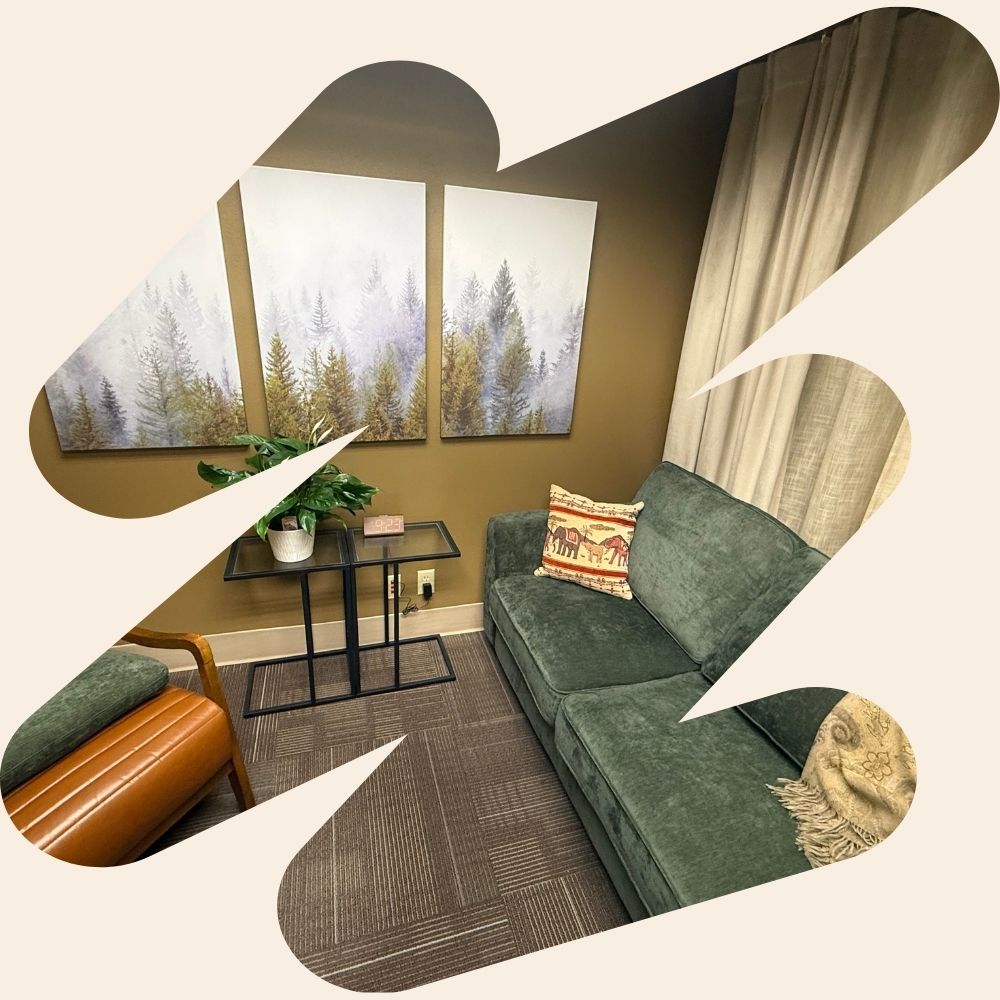 A Zoya Health Collective sitting room with a sage green sofa, leather chair, potted plant, and three evergreen forest art panels, framed by a decorative cream border